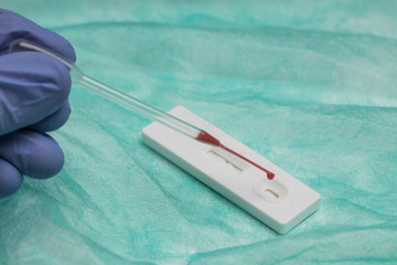 Unrecognizable medic in surgical glove examining blood sample while using pipette and professional tool for rapid test on COVID 19
