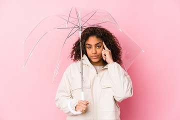 Young african american woman holding a umbrella pointing temple with finger, thinking, focused on a task.