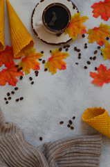 Autumn background with copy space for text and design. A cup of coffee, coffee beans waffle cones and autumn leaves. Cozy atmosphere and warm mood