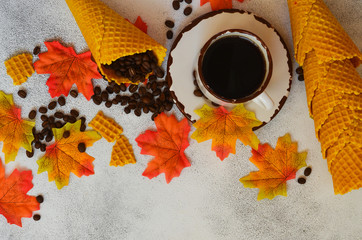 Autumn background with copy space for text and design. A cup of coffee, coffee beans waffle cones and autumn leaves. Cozy atmosphere and warm mood