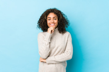 Young african american curly hair woman smiling happy and confident, touching chin with hand.