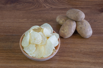 Homemade Potato Chips in bowl on wooden table. with freshly harvested organic potatoes