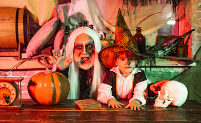 Obraz na płótnie Canvas Grandpa and grandson with pumpkin together as preparation for Halloween. Dad and his kid in carnival costumes on Halloween background. Happy Father and Children boy in Halloween Costume.