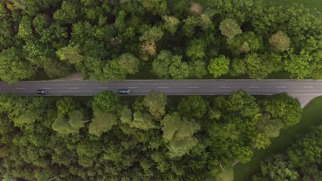 A slow tractor is drining down a street from the right to the left, filmed with a drone directly from above - flying with the tractors direction - cars a passing by the agricultural vehicle.