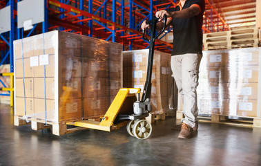 Manufacturing warehouse storage, Cargo export, Shipment. Warehouse worker using hand pallet truck unloading a large pallet goods in the warehouse.