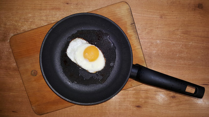 fried eggs from one egg in a black frying pan on a wooden cutting board