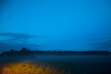 Fototapeta premium View from the road to a field with fog late in the evening or at night.