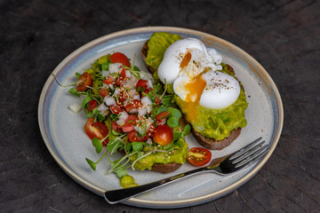 Healthy breakfast with bread toast and poached egg with green salad, red tomato and smashed avocado