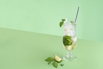 Minimalistic mojito cocktail on a green background with lime piece, mint leaves and silver straw. Photo with place for your text.