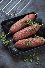 Cast-iron tray with fresh uncooked seasoned beef kabobs and charcoals, vertical shot on a grey asphalt surface