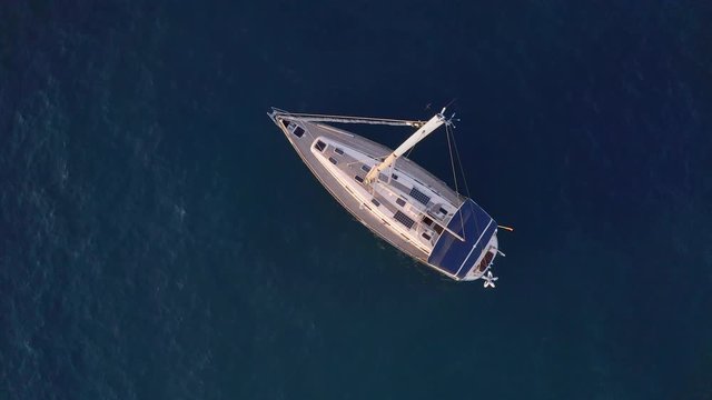 Overhead 4k shot of a luxurious private yacht with a tall mast on a dark blue sea anchoring close to a rocky coast on a sunny summer day. Luxury yacht anchoring close to shore in a tropical bay.