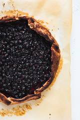 A close-up of a black currant galette on baking paper on white background, top view