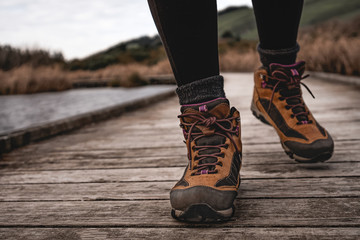 Woman's trekking boots walking on wooden walkway on autumn season. Travel concept
