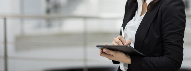 Portrait of a young cheerful businesswoman surfing social network on digital tablet in front of office during break. Asian business woman standing in office building. Stock photo