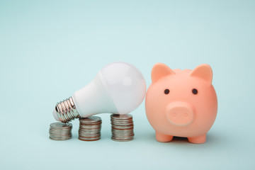 Piggy bank, stack of coins and led light lamp on blue background. Energy saving concept.