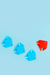 Single red origami paper fish changing direction while swimming ahead of line of blue fish. Concept for new business strategies, discovery, and different thinking