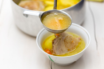 hand pours chicken soup on a white table