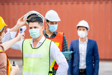 Industrial worker wear hygienic mask  and infrared thermometer at logistic warehouse container workplace,during quarantine and social distancing covid-19 pandemic illness.