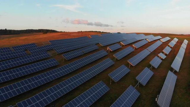 Birdseye view over a solar battery farm during sunset, near a lake.