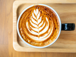 Latte milk foam art on top coffee in ceramic black cup served on wooden plate in cafe