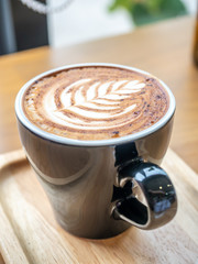 Hot milk coffe, latte, with milk foam art top, in black ceramic cup, served on wooden plate in morning cafe