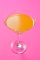 Cold summer yellow alcohol Martini cocktail in a Martini glass isolated on bright pink background.