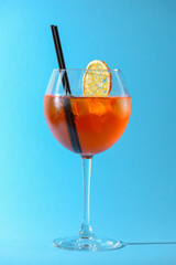 A glass of fruit liqueur in wine glass with a piece of lemon and black plastic straw isolated on pastel blue background.