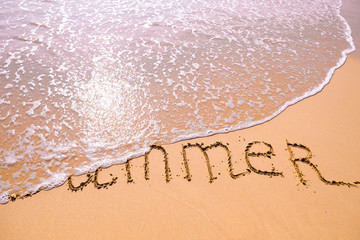 Fototapeta premium Word Summer hand written in the sand with a sea wave. Close up sand texture on beach in summer.