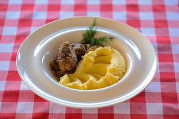 Fried fish with mashed potatoes and sauce served on a white plate over red plaid tablecloth.