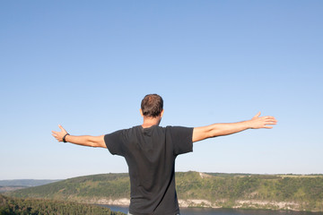 A man with arms outstretched against the backdrop of the sky and nature. Recuperation, enjoyment, balance concept