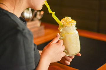 Yellow orange and lemon freakshake with sweets. Eating out concept. Young attractive woman drinking...