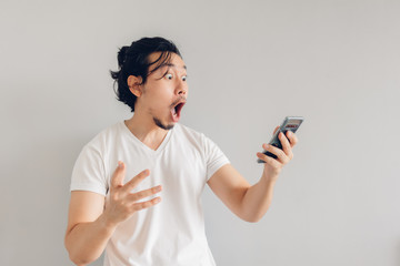 Surprised and shocked long hair Asian man in white t-shirt is using smartphone.
