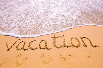 Word Vacation hand written in the sand with a sea wave. Close up sand texture on beach in summer.