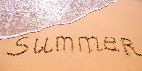 Word Summer hand written in the sand with a sea wave. Close up sand texture on beach in summer.
