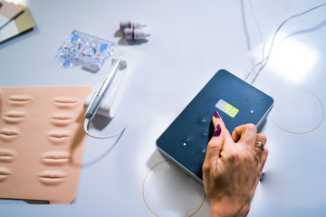 Master of permanent tattoo with tool for micro blading, training in permanent makeup on false lips.