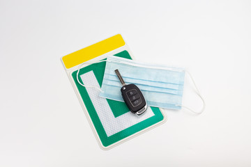View of a green Spanish driving school license plate with a protective mask and a car key on a white background, for covid-19 pandemic prevention  