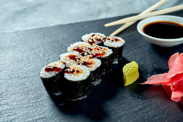 Appetizing maki sushi with eel on a black slate board