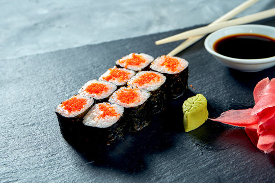 Appetizing maki sushi with tobico caviar on a black slate board