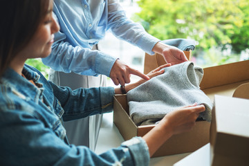 Two young women receiving and opening a postal parcel box of clothing at home for delivery and...