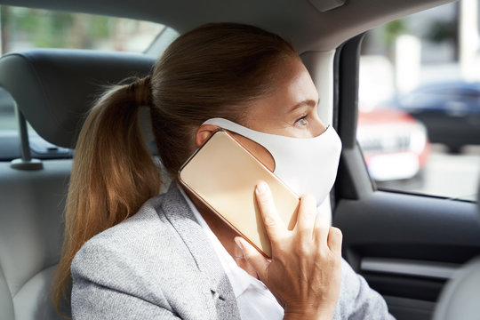 Business during coronavirus. Business woman wearing protective face mask talking by mobile phone while sitting on back seat in the car