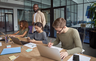 Successful business people. Group of young multiracial people, coworkers working together in modern office, using laptops, smartphone, making some notes