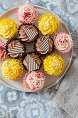 Variety of cupcakes on a grey plate.  Blue patterned tile background