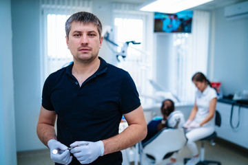 Naklejka na ściany i meble Male dentist in latex gloves in front view. female doctor and patient on front background.