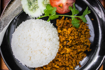 Thai Stir-fried pork with yellow curry paste on white rice served on black dish.