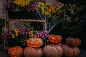 Happy Halloween. Spooky Jack-o'-lantern with glowing faces and cobweb in dark. Pumpkins with scary carved faces and candle light, modern festive halloween street decor.