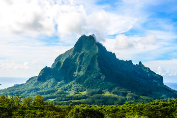 Fototapeta premium Moorea, French Polynesia: 09/03/2018: Total lanscape of the colorful main mountain in Moorea, everywhere is green and a blue sky