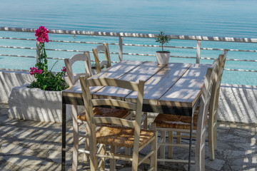 Fototapeta na wymiar Chalkidiki, Greece empty tavern wooden chairs & table after new covid-19 measures. Restaurant outdoor seating area by the sea without customers in Kryopigi, Kassandra peninsula.