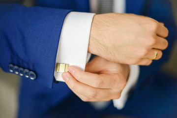 Groom or businessman fasten cufflink on the cuff of the shirt wearing blue suit