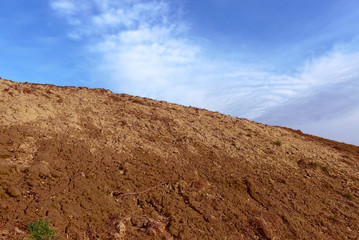The slope of a clay hill against the backdrop of a beautiful blue sky. Lifeless soil. Sunny weather. Landscape.
