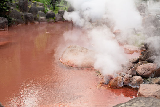 natural red colored hot spring with rising steam in beppu city, oita pref, japan